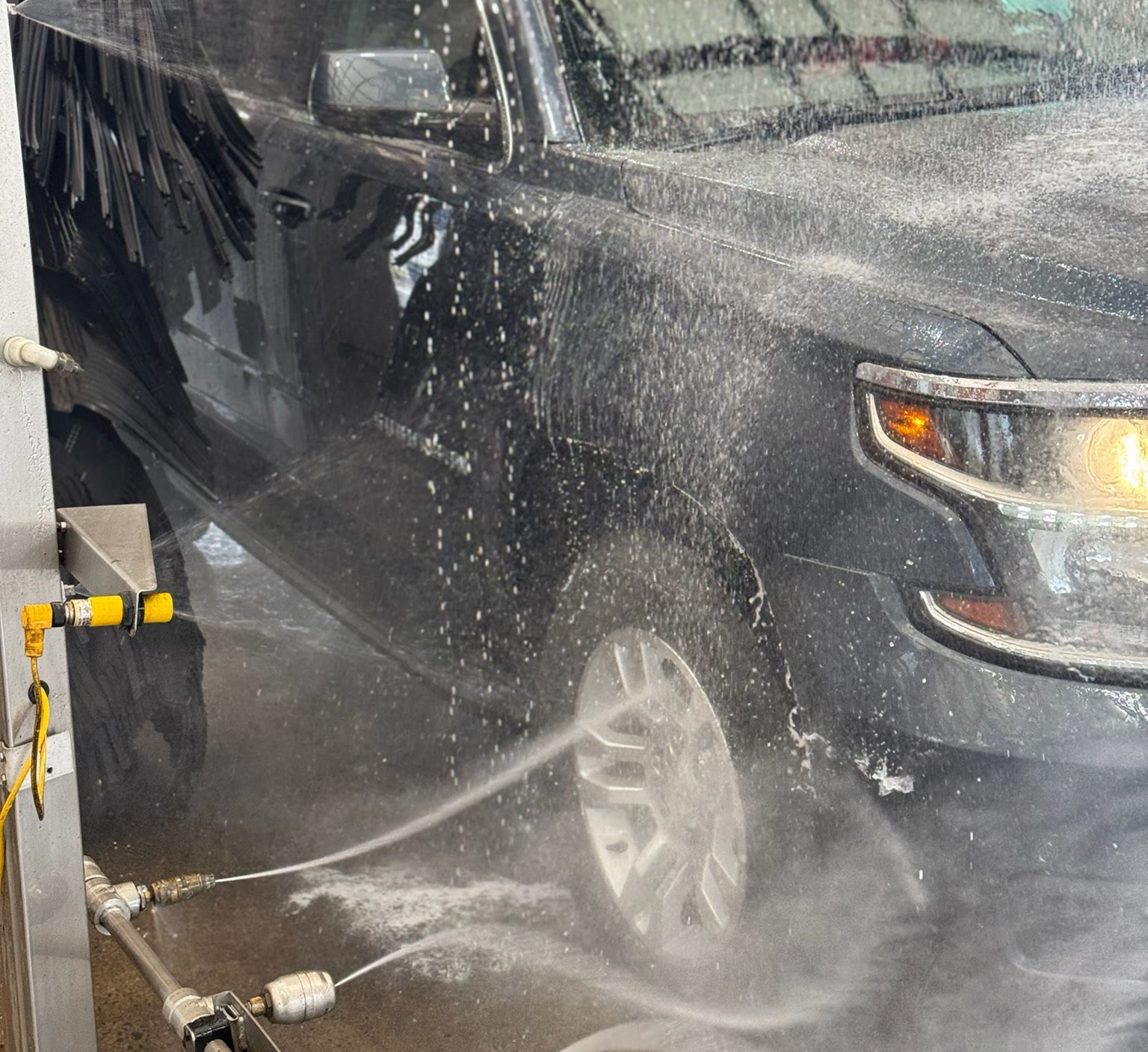 A close up photo of a black truck getting car wash wheel treatment at Clean Car Wash and Detail in Fredericksburg, VA.