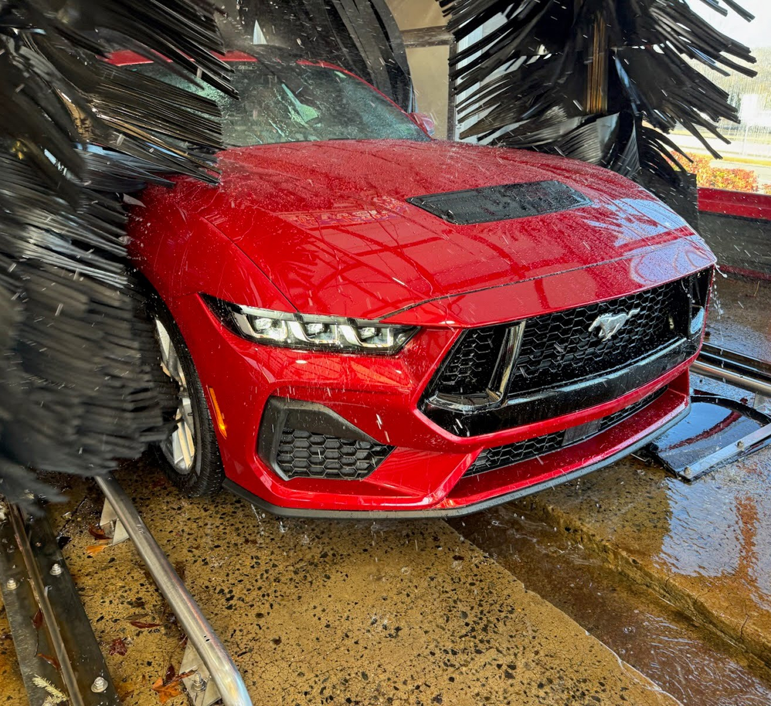 A close up photo of a red sports car running through car wash brushes at Clean Car Wash and Detail in Fredericksburg, VA.
